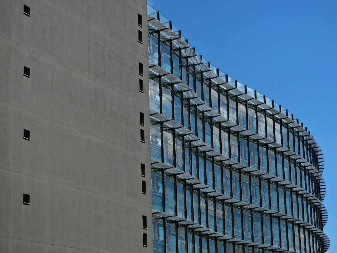 A contemporary high-rise building with a striking glass facade against a clear blue sky.
