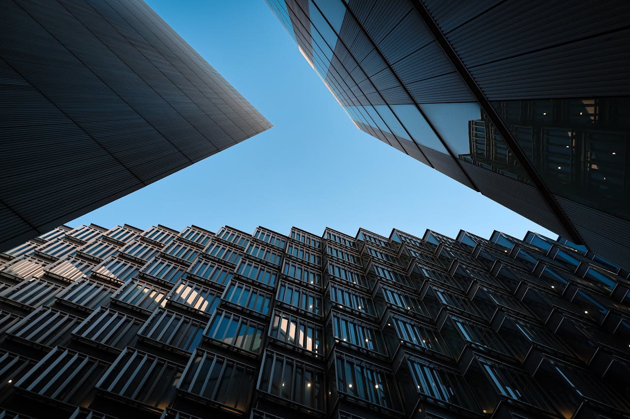 Low angle view of modern skyscrapers with glass panels reflecting under a blue sky.